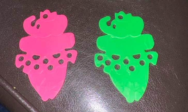 A pink and a green plastic figure with holes in them kept on a leather surface.