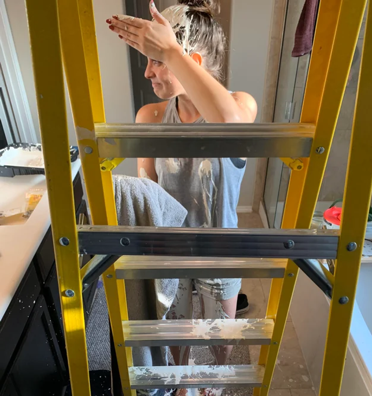 Woman in front of a ladder with paint all over her.