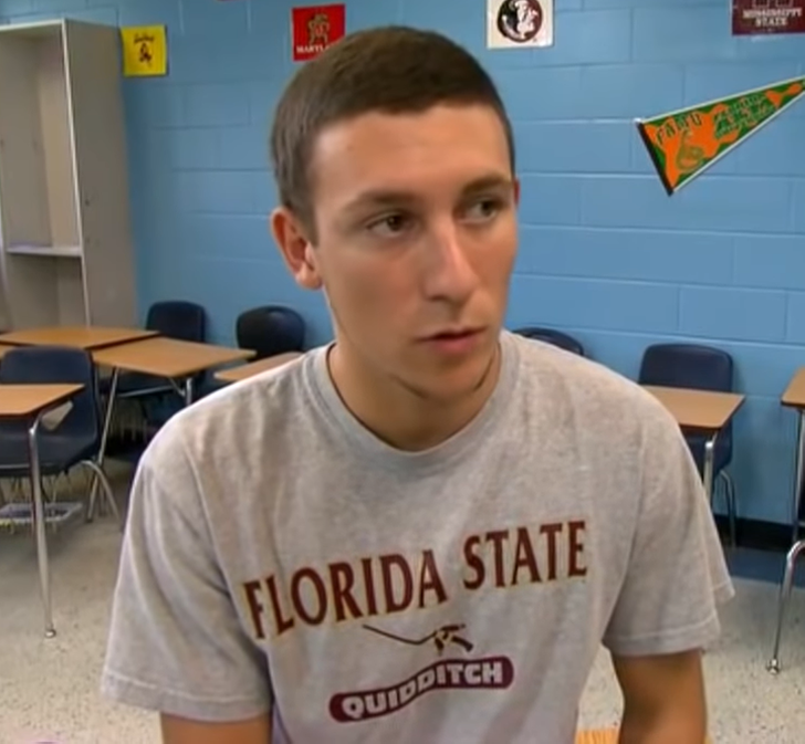 Young man sitting in a classroom with a Florida State Quidditch grey t-shirt.