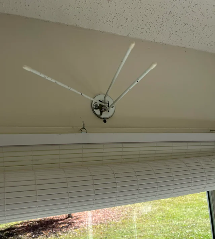 A window with white blinds and hinged rods above it.