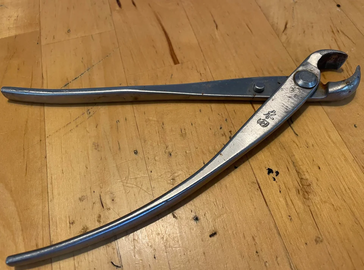 A scissor-looking metal tool on a wooden table.