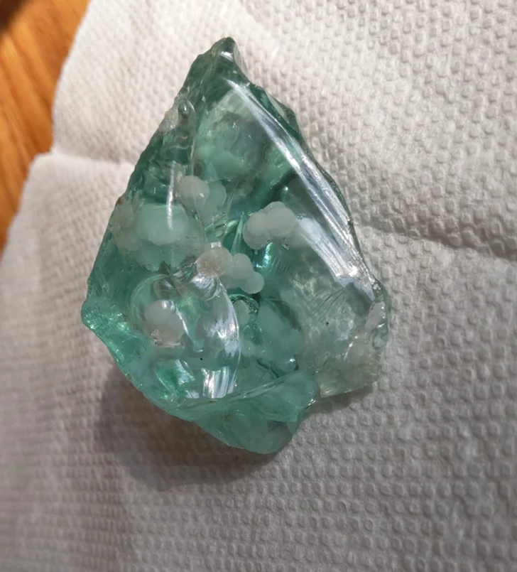 A lump of green glass with white spots in it. It has sharp and smooth edges.