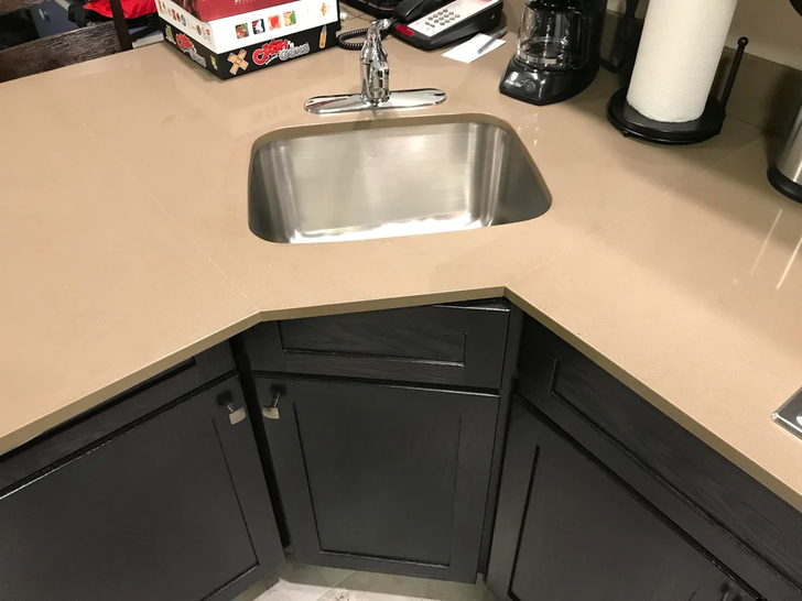 Misaligned kitchen counter with sink and dark cabinets.